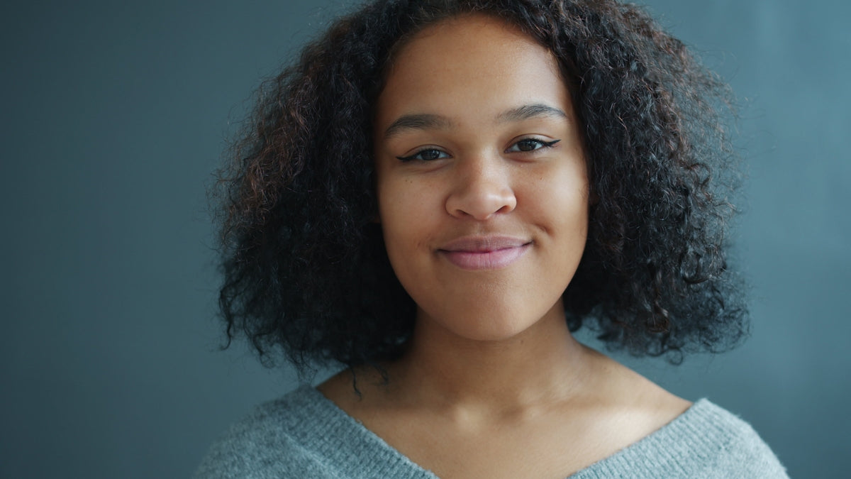A young black woman with curly hair smiles.
